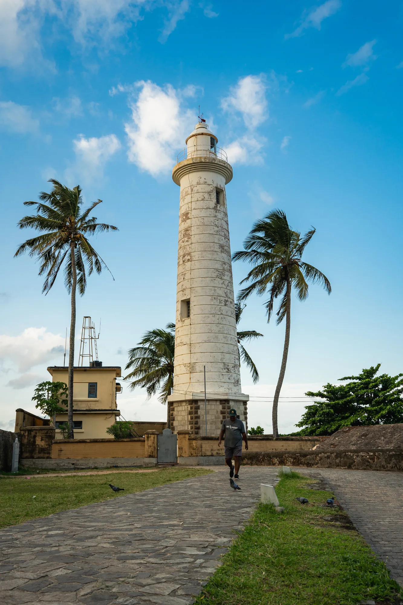 En besökare går mot fyren i Galle Fort under palmerna.